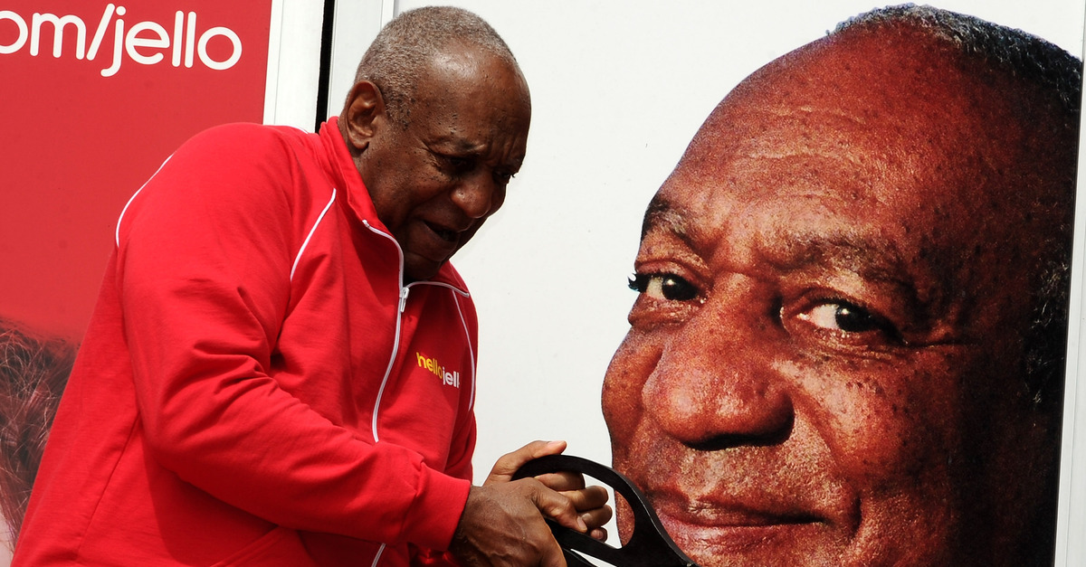 Bill Cosby appears in front of a photo of his face