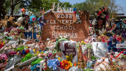The Robb Elementary School sign is seen covered in flowers and gifts on June 17, 2022 in Uvalde, Texas. (Photo by Brandon Bell/Getty Images.)