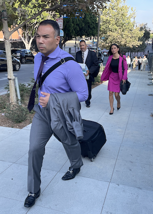 A man in a shirt and tie who is pulling a briefcase as he leaves his criminal trial in downtown Los Angeles