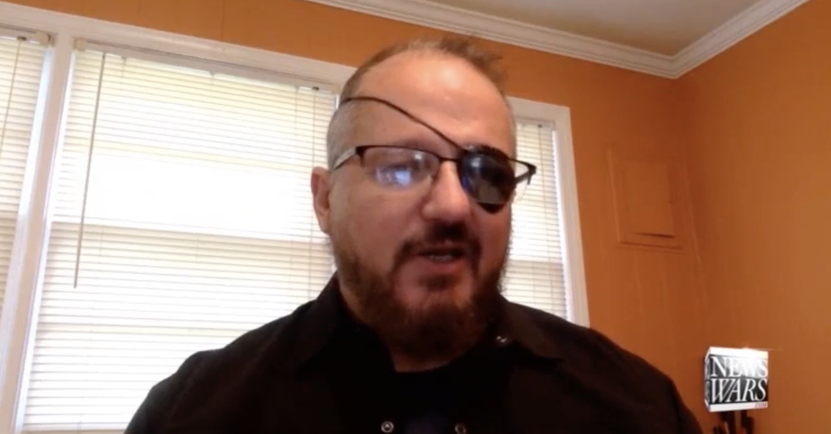 Stewart Rhodes, wearing glasses and an eyepatch, in a room with orange walls and a window, gives a video interview to Alex Jones of InfoWars (via FBI trial exhibit screengrab).