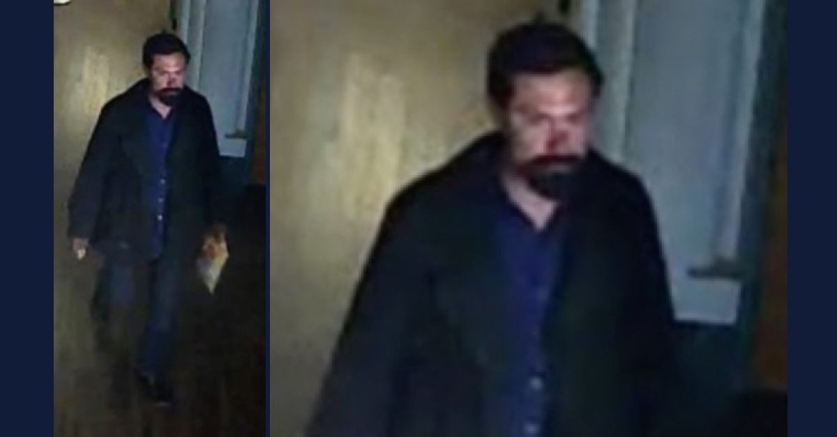 A man with dark hair, beard, and mustache is seen on surveillance camera.