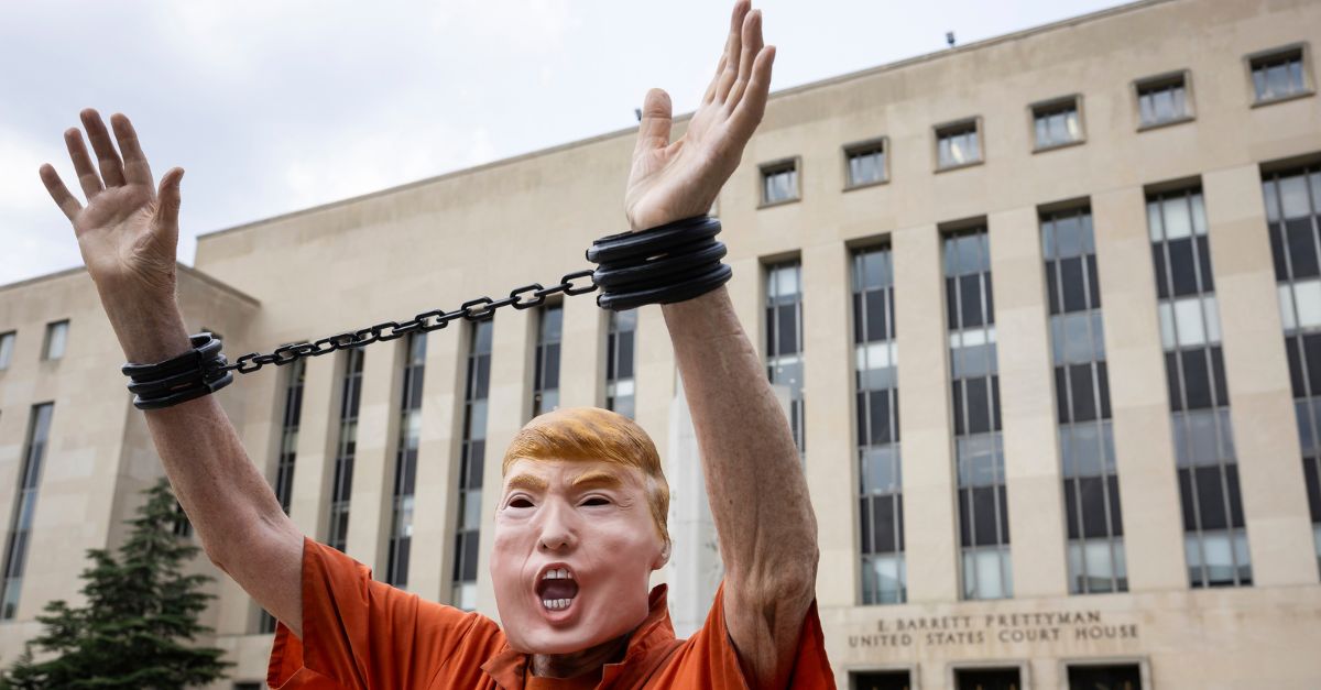 A man wearing a Donald Trump mask appears outside of a federal courthouse with an orange jumpsuit and fake handcufffs on.